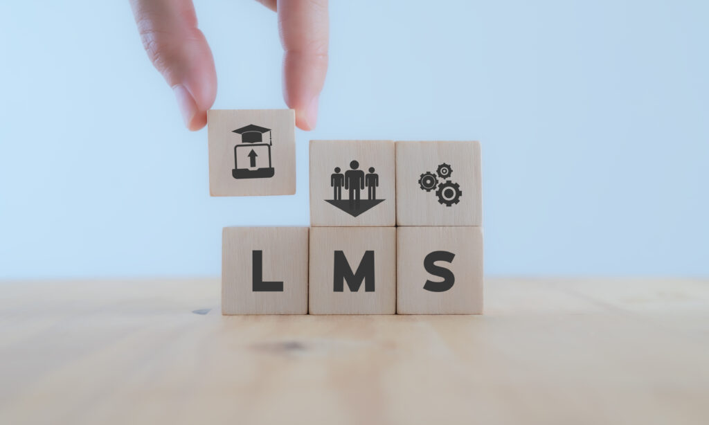 LMS Learning Management System concept.  Hand holds wooden cube with LMS symbols on beautiful light background with copy space. 